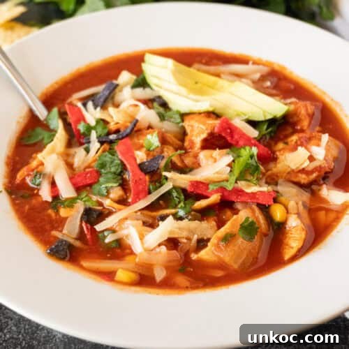 Chicken tortilla soup in a white bowl garnished with avocado, chips, and green onions.