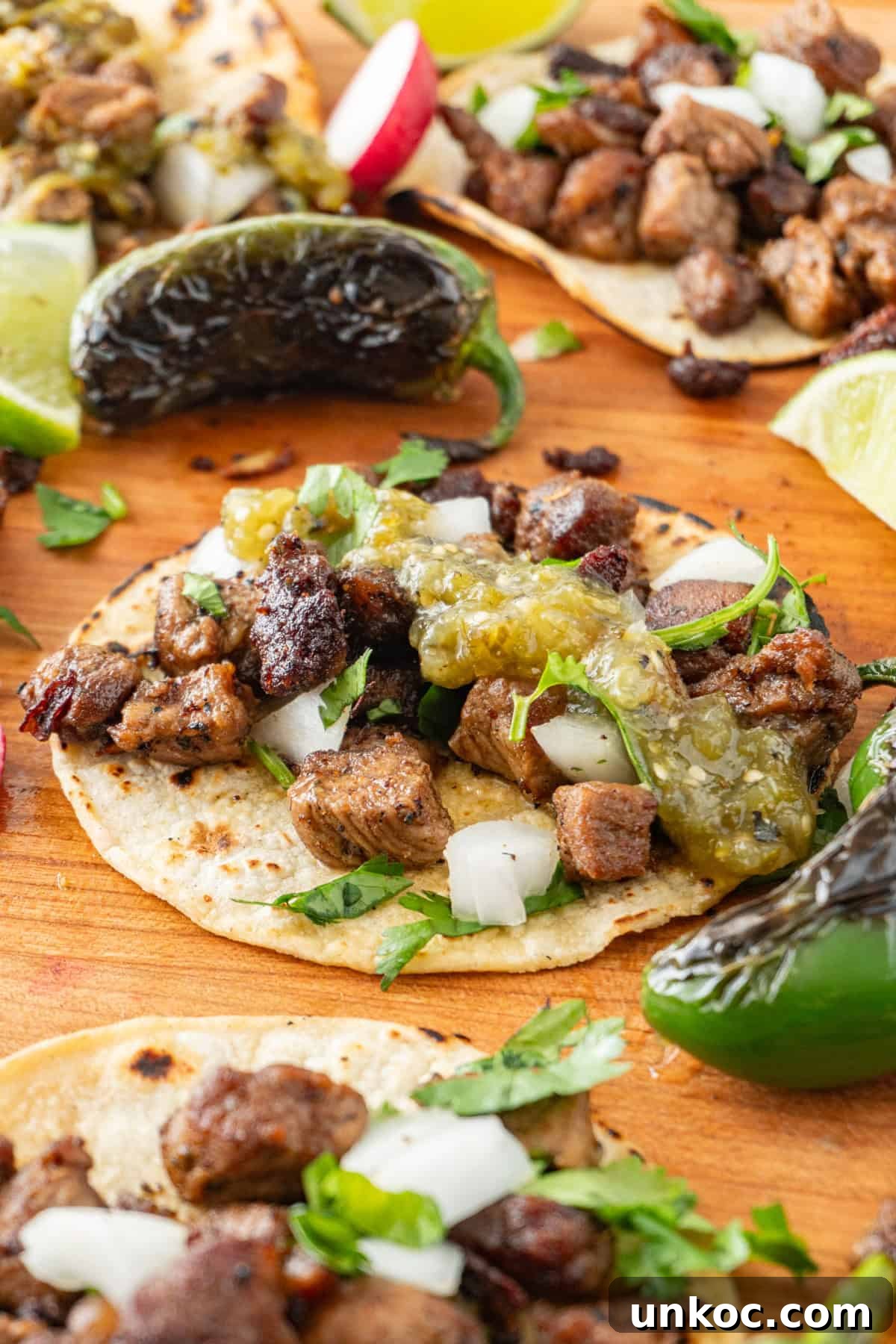 Taco topped with tomatillo salsa, sprinkled with onion and cilantro on a cutting board surrounded by blackened jalapeno and lime wedges.