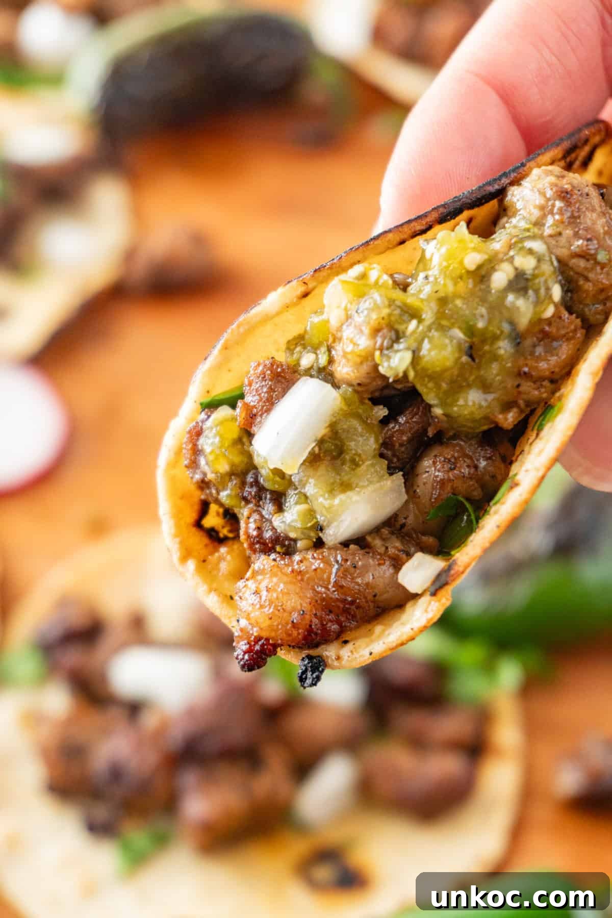 Holding a street taco with roasted tomatillo salsa on it.