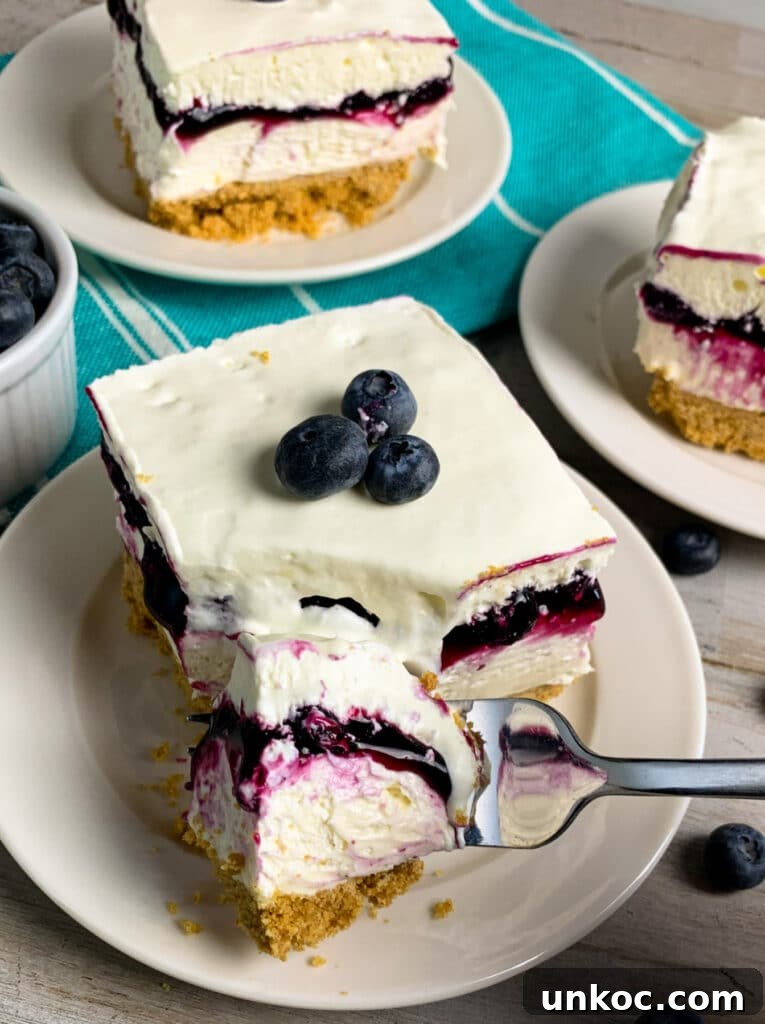No-bake blueberry cheesecake bars on a white plate and being picked up with a fork.