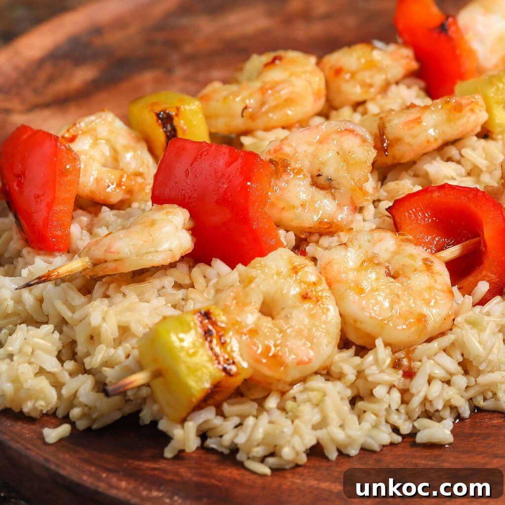 Spicy Honey Glazed Shrimp and Pineapple Skewers 2 Shrimp Pineapple Skewers with a Spicy Honey Glaze, paired with red bell peppers and served on a bed of brown rice on a wooden plate.