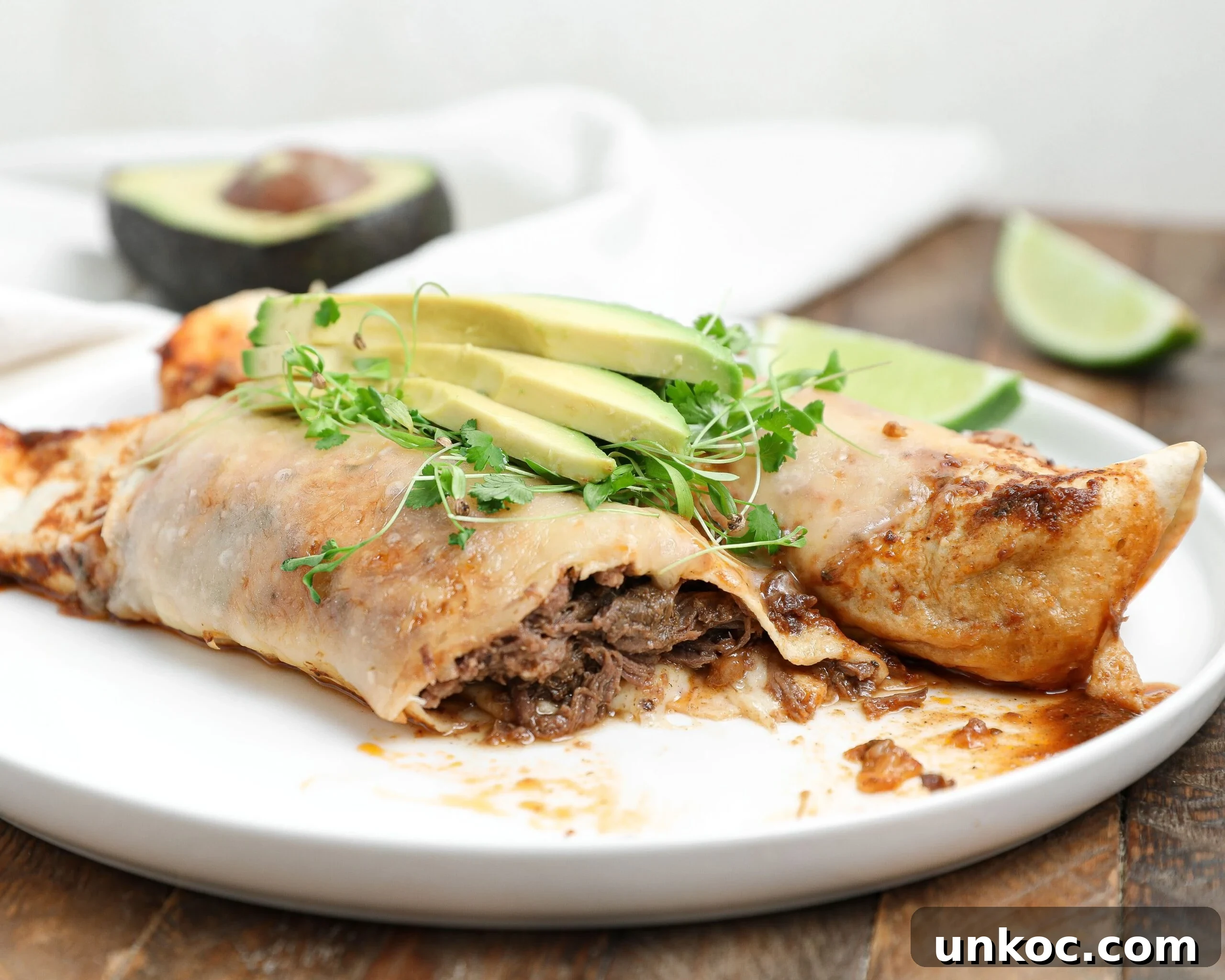 Spicy Honey Glazed Shrimp and Pineapple Skewers 11 Plate of beef barbacoa enchiladas topped with avocado slices and microgreens, with lime wedges and half an avocado in the background.