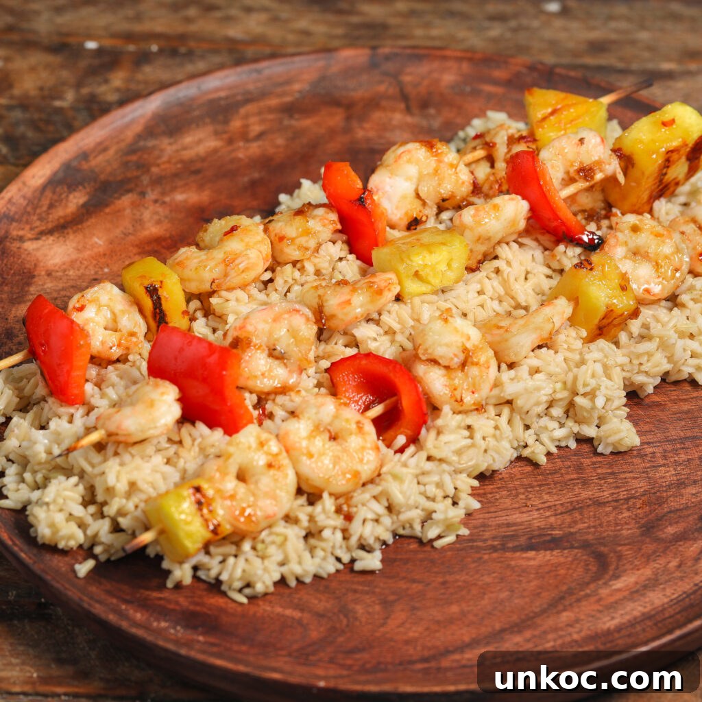 Spicy Honey Glazed Shrimp and Pineapple Skewers 4 Shrimp Pineapple Skewers with a Spicy Honey Glaze, paired with red bell peppers, are served on a bed of brown rice atop a wooden plate for a vibrant, flavorful meal.