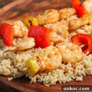Spicy Honey Glazed Shrimp and Pineapple Skewers 5 Shrimp Pineapple Skewers with a Spicy Honey Glaze, paired with red bell peppers and served on a bed of brown rice on a wooden plate.
