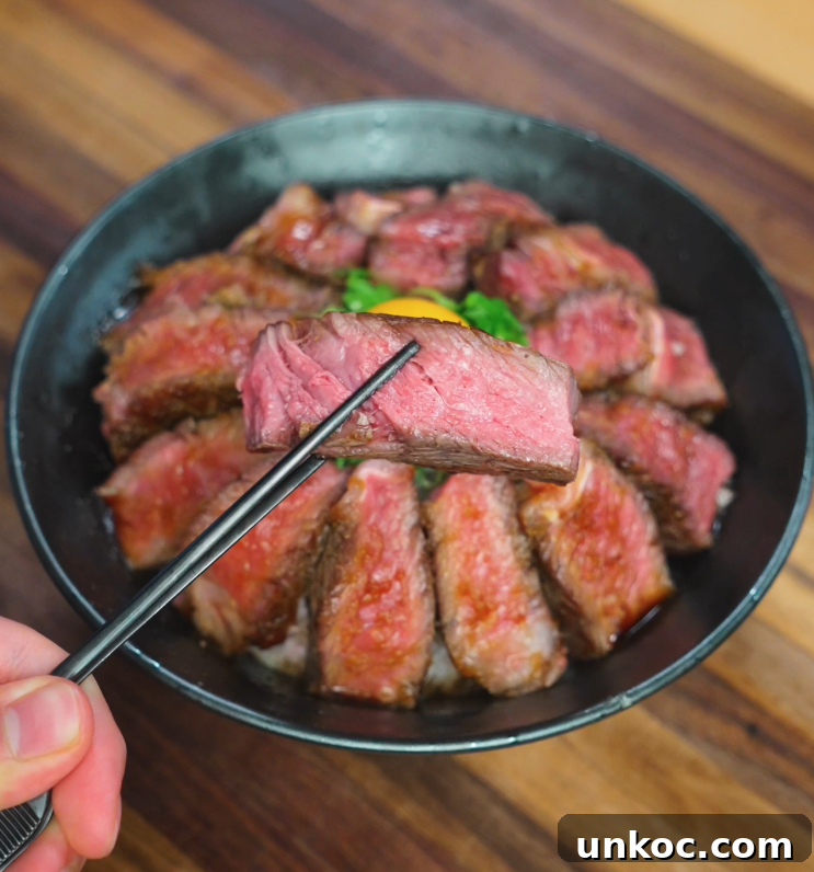 Japanese Steak Donburi Rice Bowl Recipe 3 Chopsticks holding a juicy, medium-rare slice of steak above a rice bowl topped with egg yolk and scallions.
