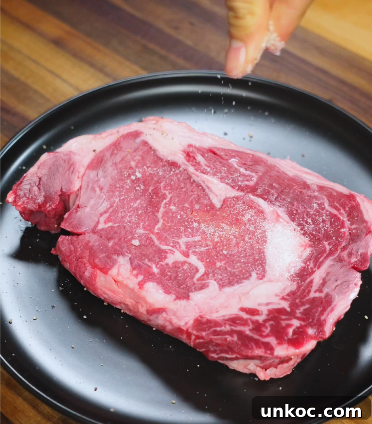 Japanese Steak Donburi Rice Bowl Recipe 4 Hand sprinkling salt over a raw, marbled ribeye steak on a black plate before searing for steak rice bowl.