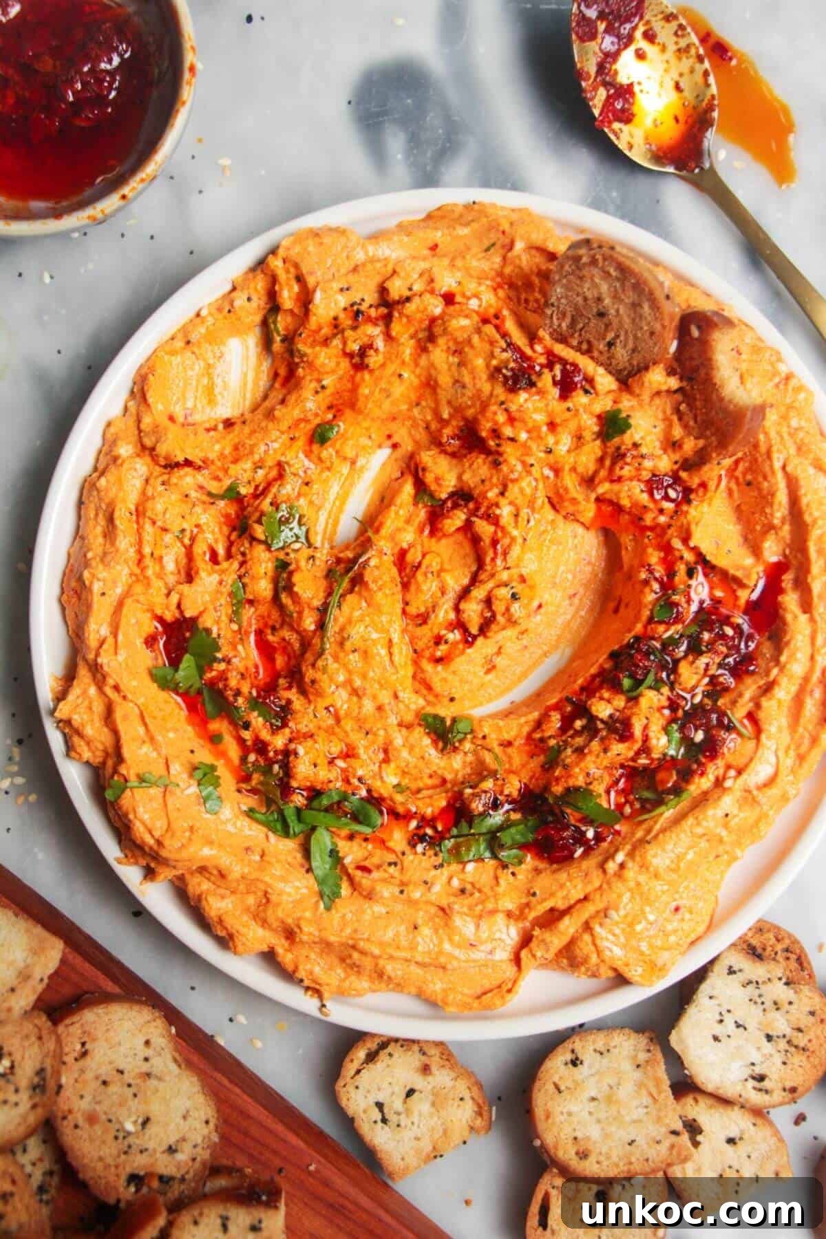 Spicy Harissa Whipped Feta Dip 2 Spicy harissa feta dip on a small white plate, with bagel chips and more harissa on the side.