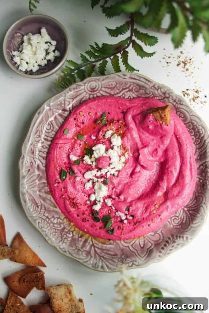 Spicy Harissa Whipped Feta Dip 11 Bright pink beet feta dip on a pink plate with feta crumbled on top and pita chips on the side.