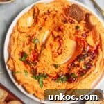 Spicy harissa feta dip on a small white plate, with bagel chips and more harissa on the side.