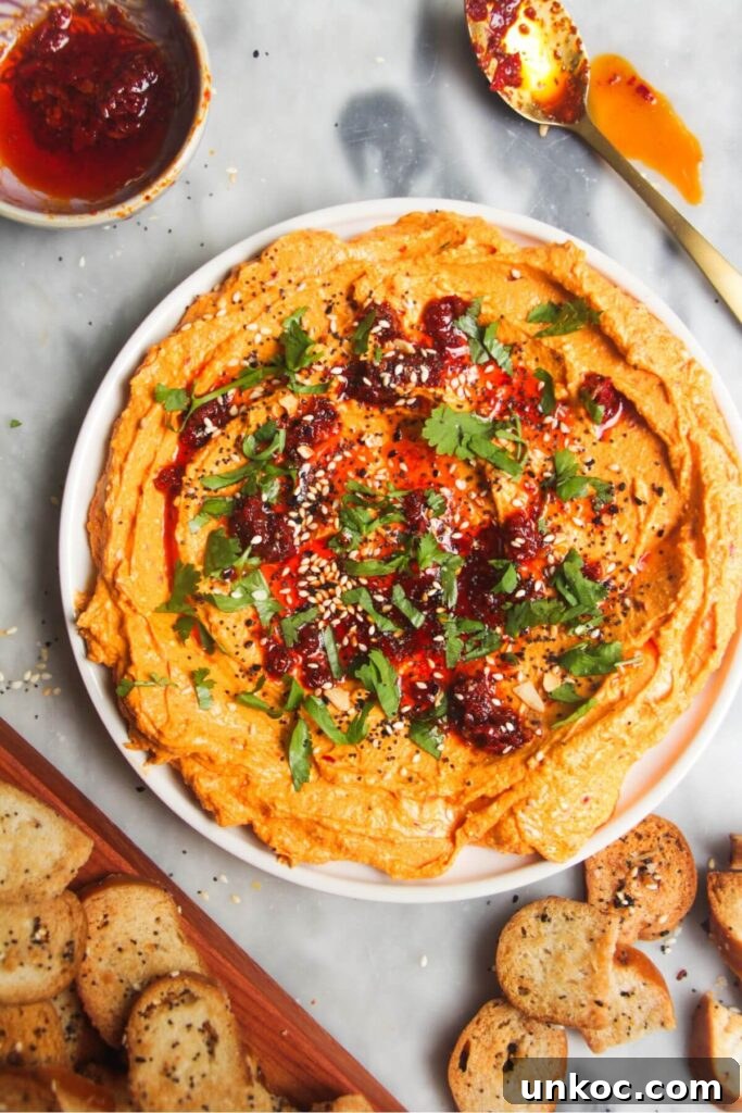 Spicy Harissa Whipped Feta Dip 7 Spicy harissa feta dip on a small white plate, with bagel chips and more harissa on the side.