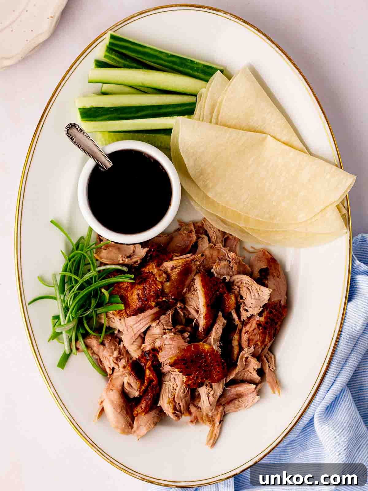 A platter with cooked slow cooker duck shredded, Chinese pancakes, cucumber, spring onion and sauce.
