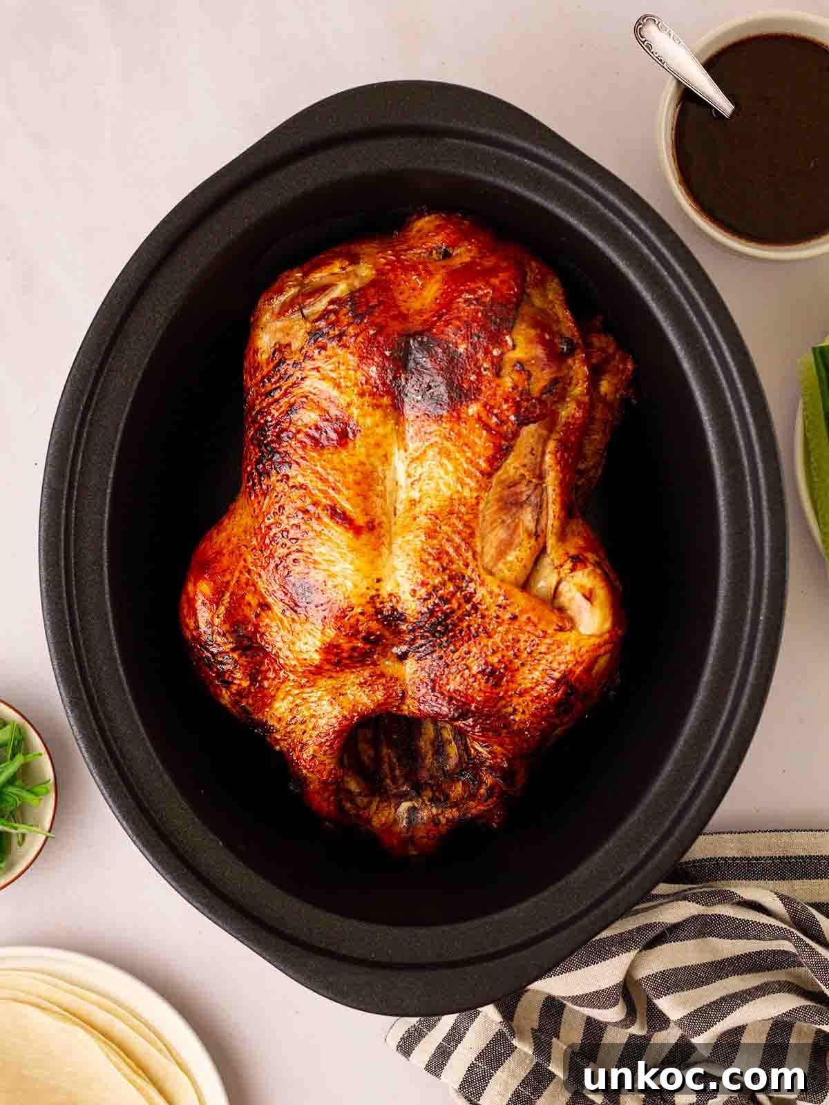 A slow cooker with a browned duck inside for Peking Style Duck recipe. A bowl of sauce to the side.