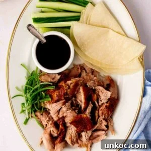 A platter with Peking style crispy duck, cooked in the slow cooker, with pancakes, sauce and cucumber and spring onion on the side.