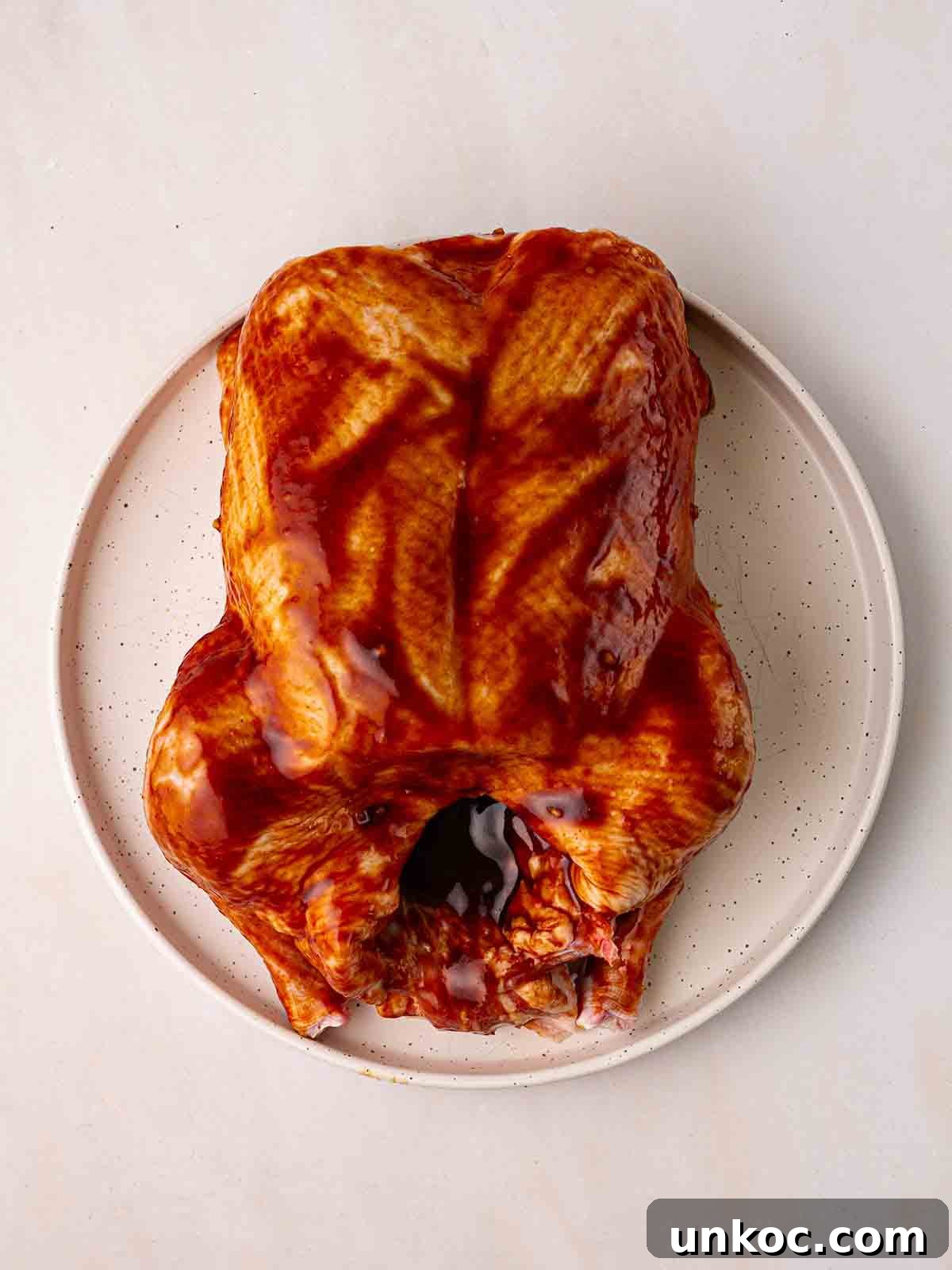 A plate with a raw duck, coated in peking sauce, ready to be cooked.