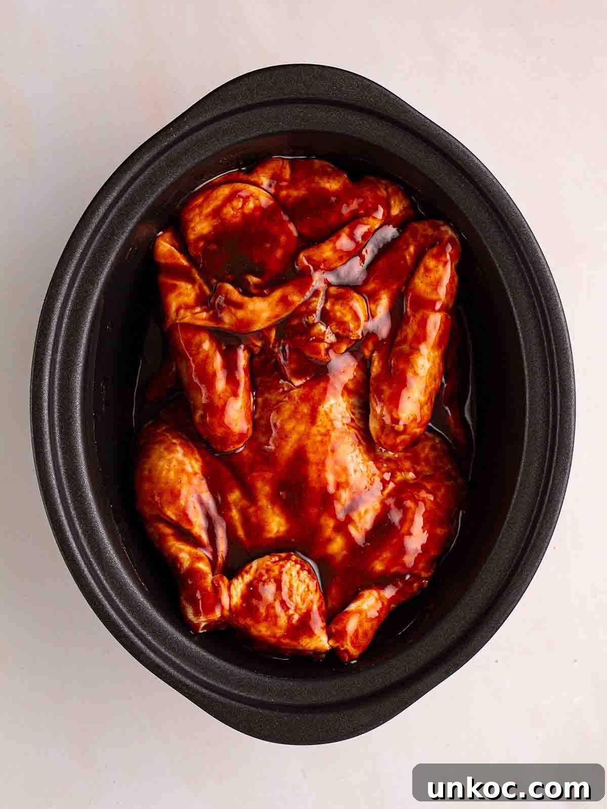 A sauce coated duck upside down in a slow cooker, ready to be cooked.