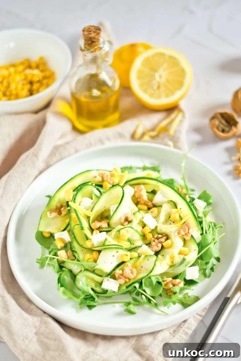 Fresh Summer Zucchini Salad with Lemon and Herbs 2 Zucchini and corn salad arranged on a white plate, with oil, lemons, and walnuts in the bacground.