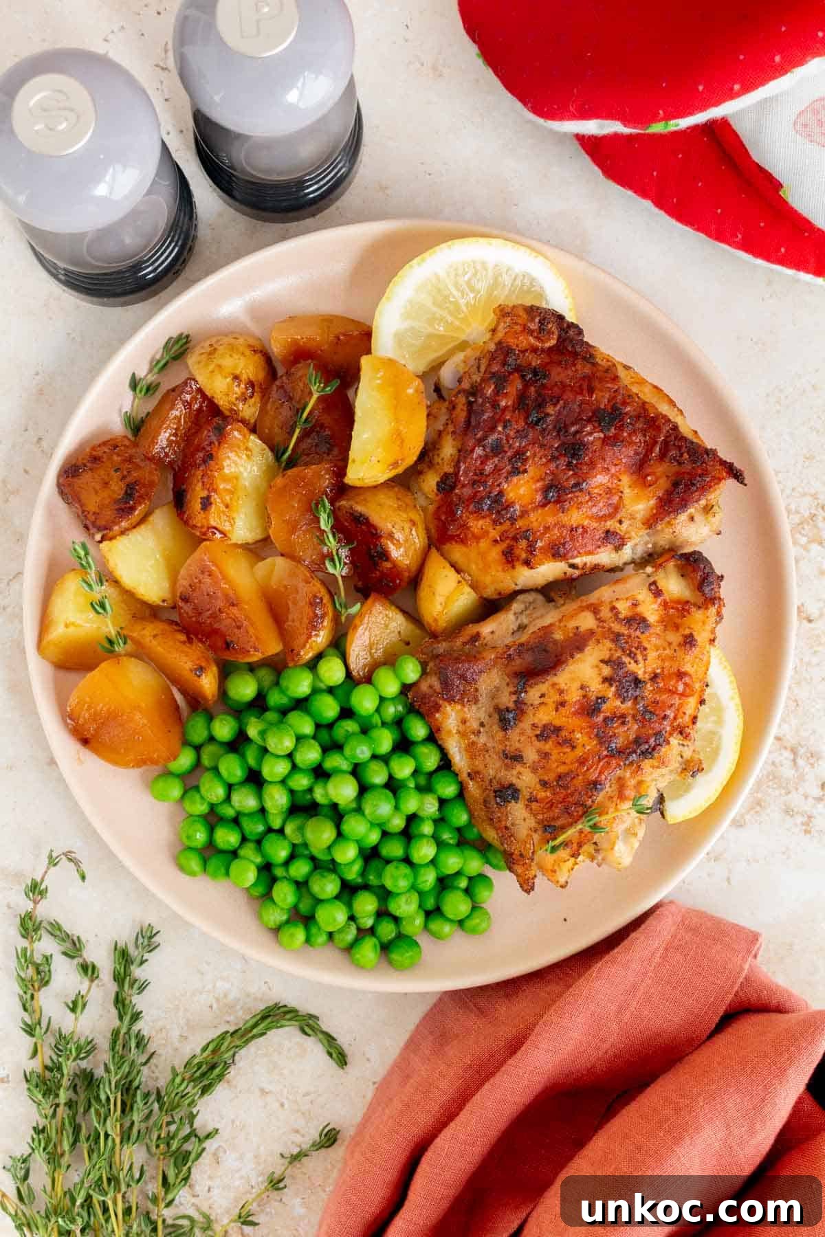 Crispy Cast Iron Chicken Thighs with Potatoes 7 A plate with cast iron chicken thighs and potatoes along with peas and lemon slices.