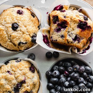 Muffins in a muffin tin. One has a wrapper removed and lays on the side.