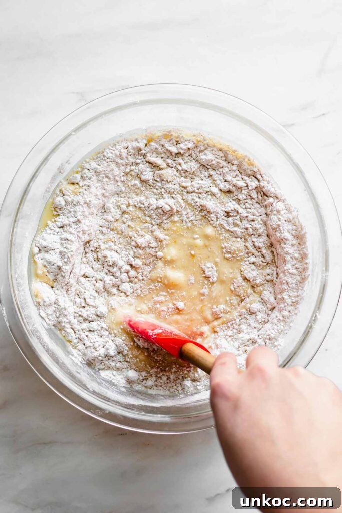 Wet and dry ingredients getting mixed together with a rubber spatula.