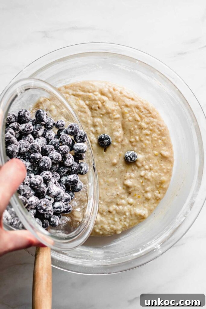 Floured blueberries getting poured into the mixed muffin batter.