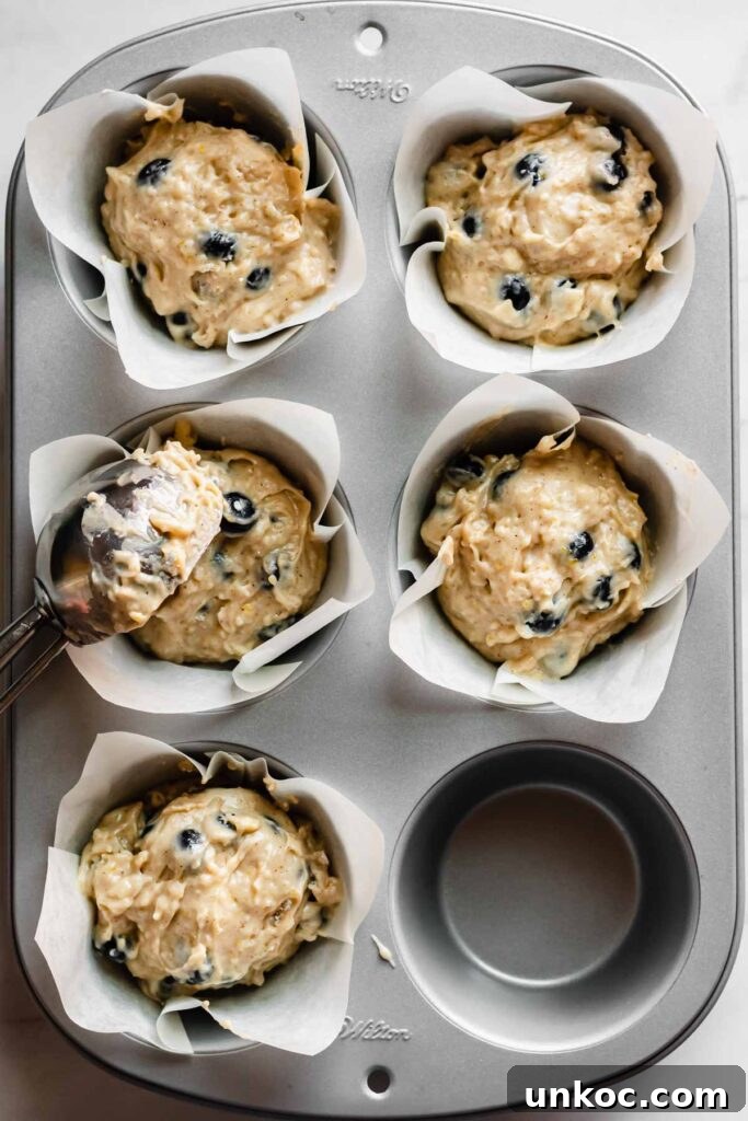 Muffin batter getting scooped into the wells with a large cookie scoop.