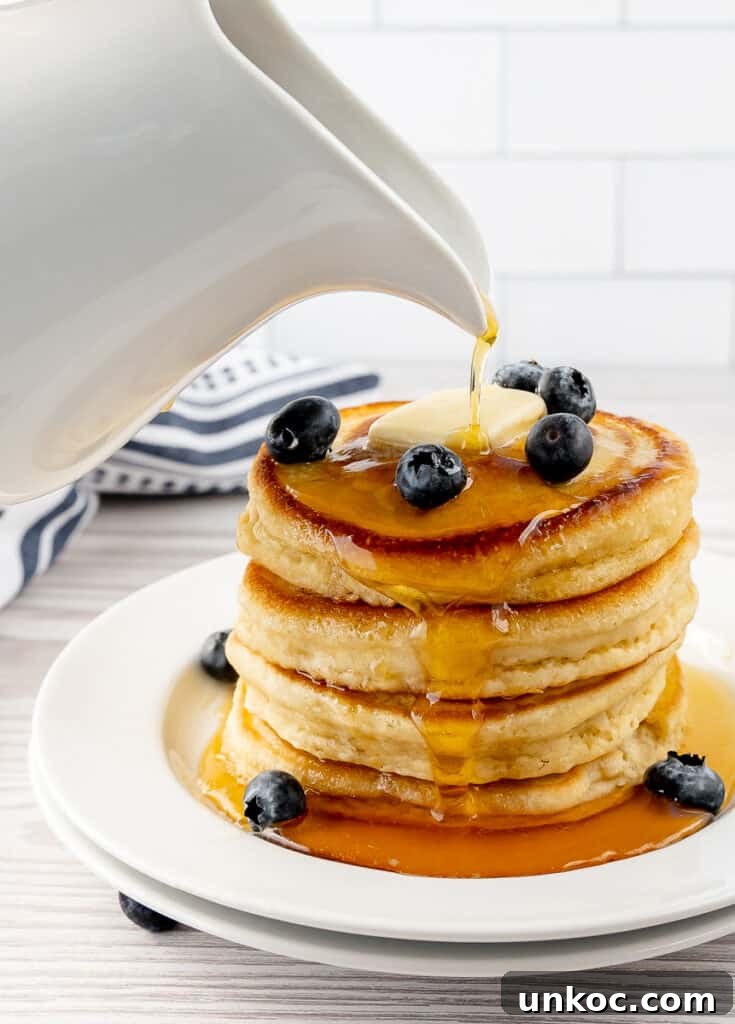 Fluffy Oat Milk Pancakes Recipe 4 Maple syrup poured over a stack of fluffy oat milk pancakes with butter and blueberries