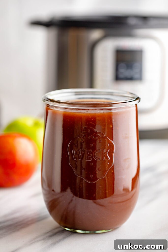 Instant Pot Apple Butter Recipe No Peeling Required 2 weck jar filled with apple butter with a red and green apple in the background along with an instapot