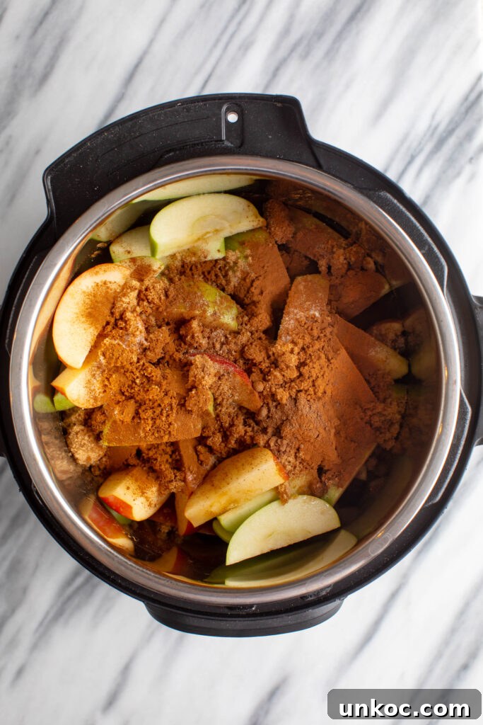 Instant Pot Apple Butter Recipe No Peeling Required 5 instapot with sliced red and green apples topped with water, brown sugar, cinnamon and salt